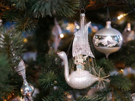 Glasfigur in Schwanenform mit Segel und Engelchen als Oblate hängt im Weihnachtsbaum.