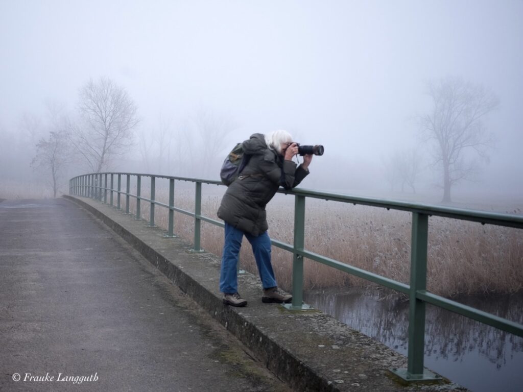 Eien Frau fotografiert mit großem Zoom von einer Brücke aus. Überall dichter Nebel.